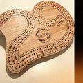 Solid wood 29-shape cribbage board with metal counting pins and engraved logo, top-down view