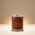 Leather-wrapped hip flask custom engraved with a monogram, front view on dark wood surface