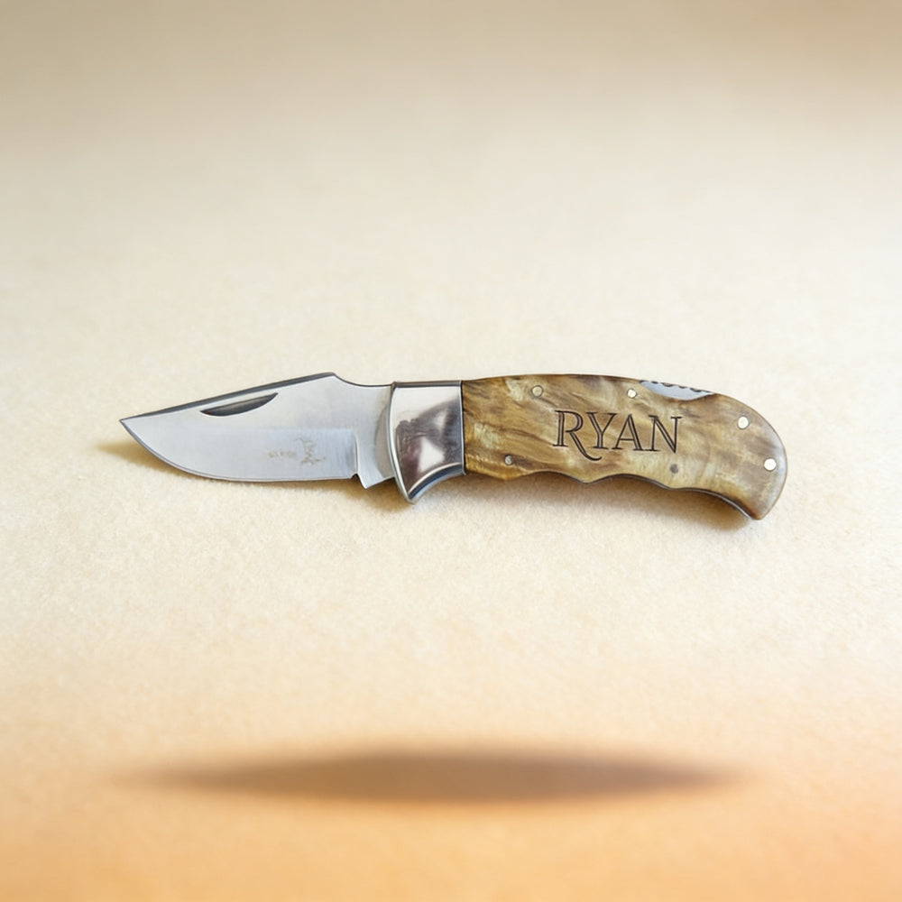 Custom engraved pocket knife with monogram, shown closed on a dark wood surface